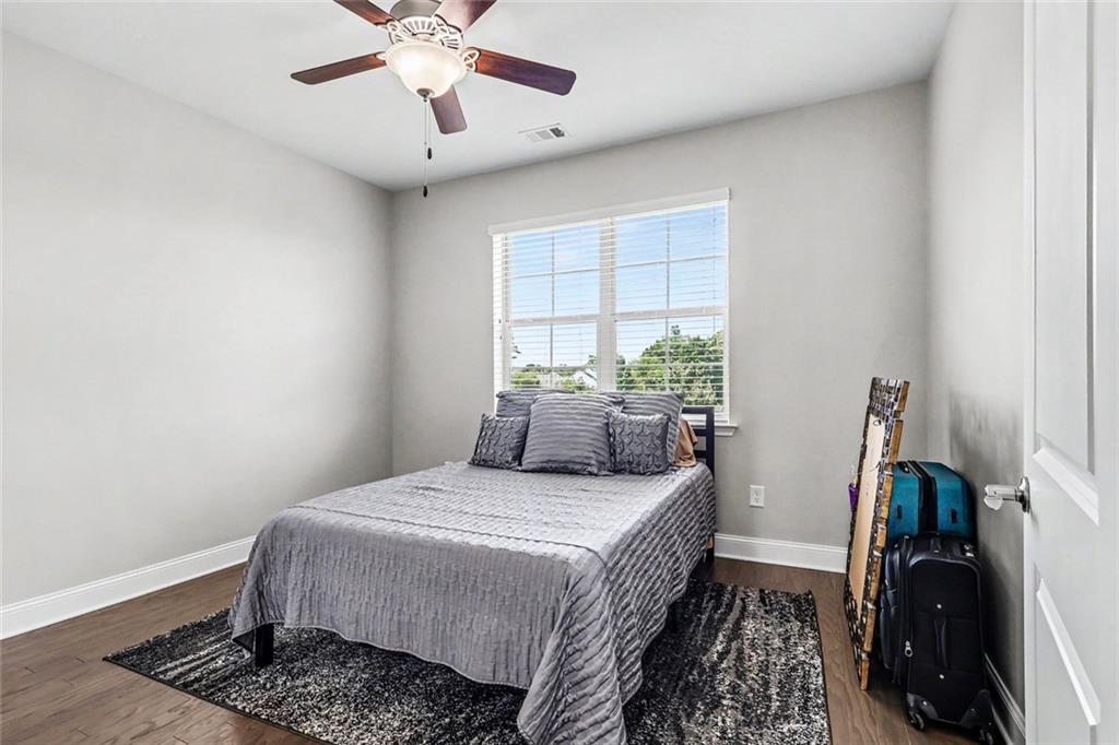 Bedroom with a gray bed, patterned rug, ceiling fan, and suitcases beside the door.