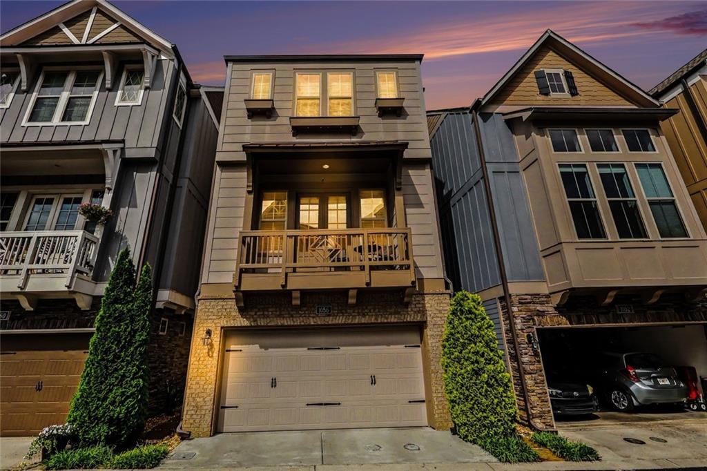 Modern townhouse with a second-floor balcony and two-car garage at dusk.
