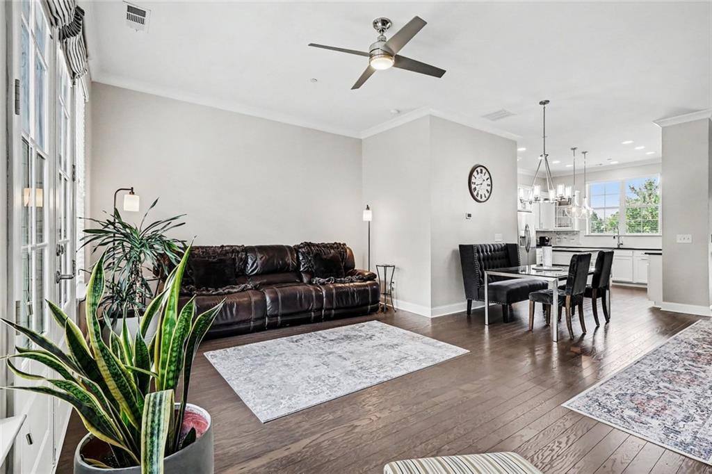 Open-plan living and dining room with a dark leather sofa, hardwood floors, and adjoining white kitchen.