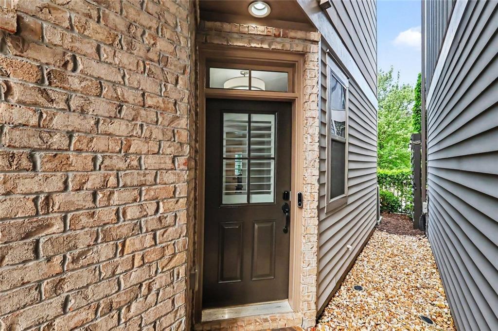 Home entrance with a dark glass-paneled door, brick walls, and a narrow gravel side walkway.