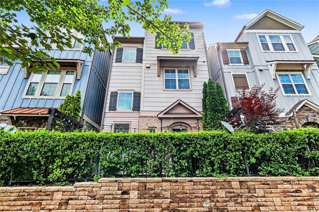 Attached multi-story homes behind a tall hedge and stone retaining wall.