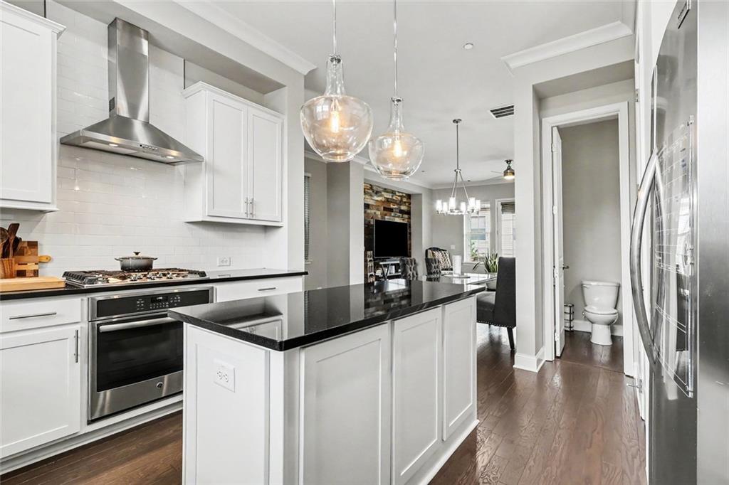 Open kitchen with a black island, stainless steel range, and glass pendant lights; living area visible beyond.