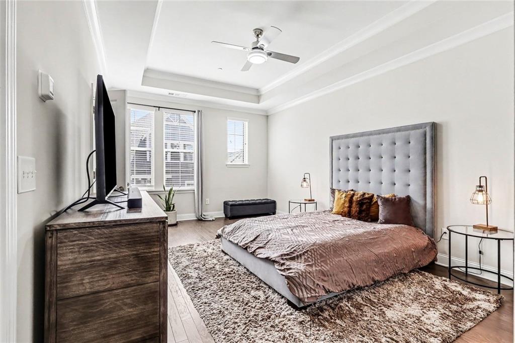 Furnished bedroom with a tufted gray headboard, tall windows, and a large textured rug.