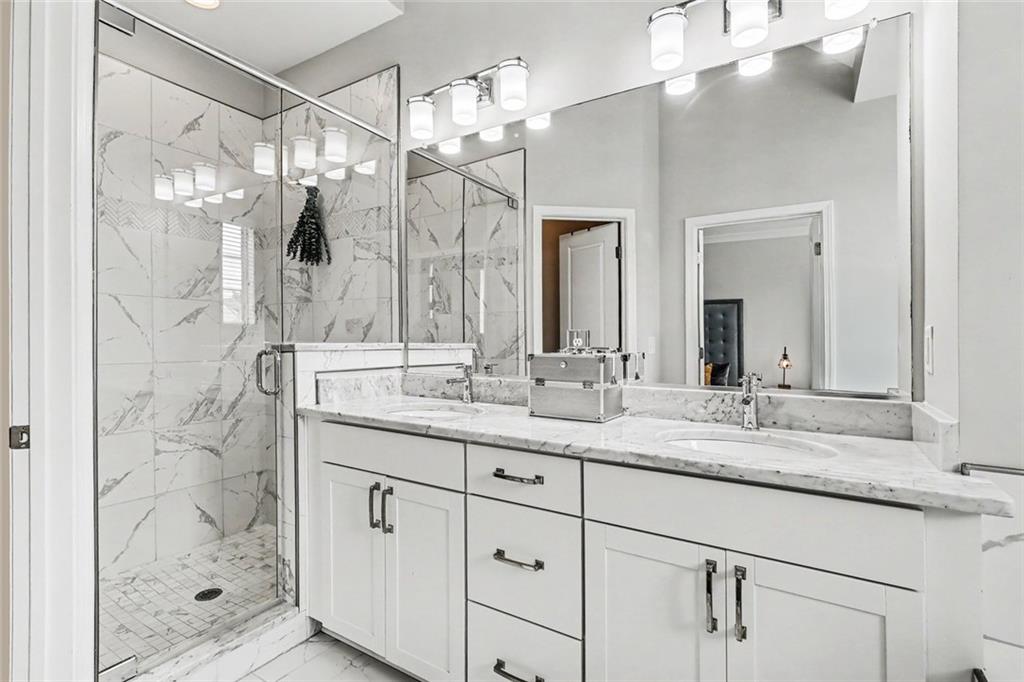 Bathroom with a double-sink vanity and a glass-enclosed marble-tile shower.
