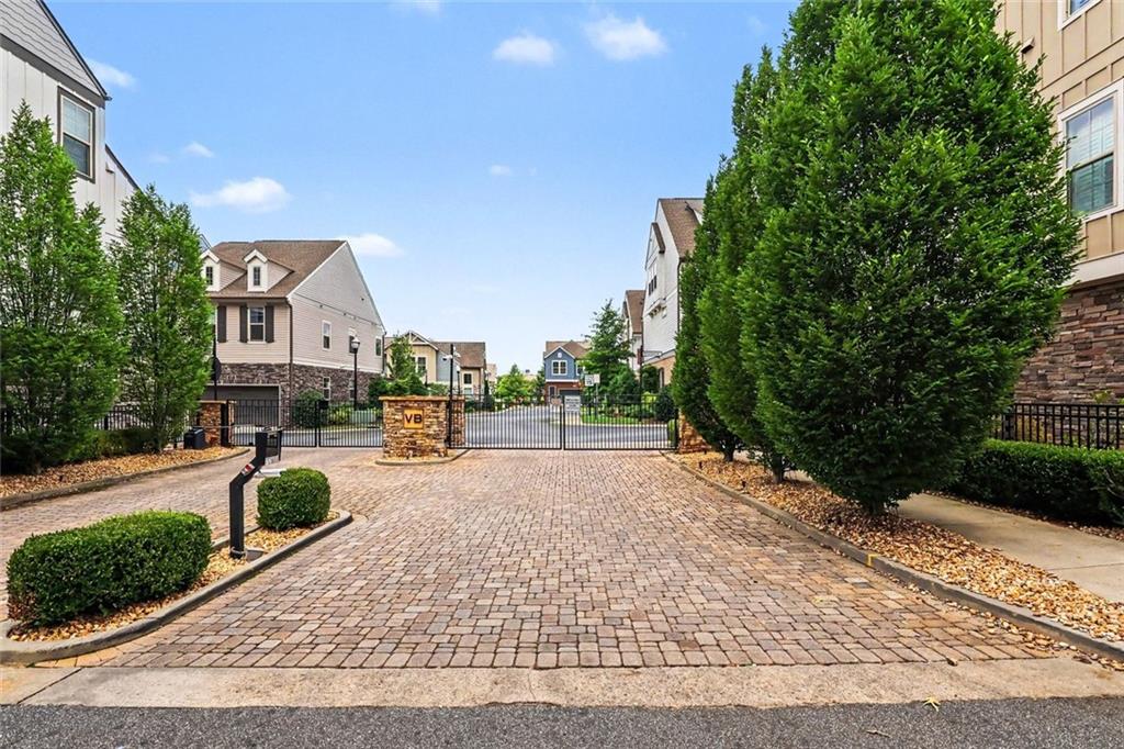 Gated townhouse entrance with a brick-paved drive and landscaped shrubs.
