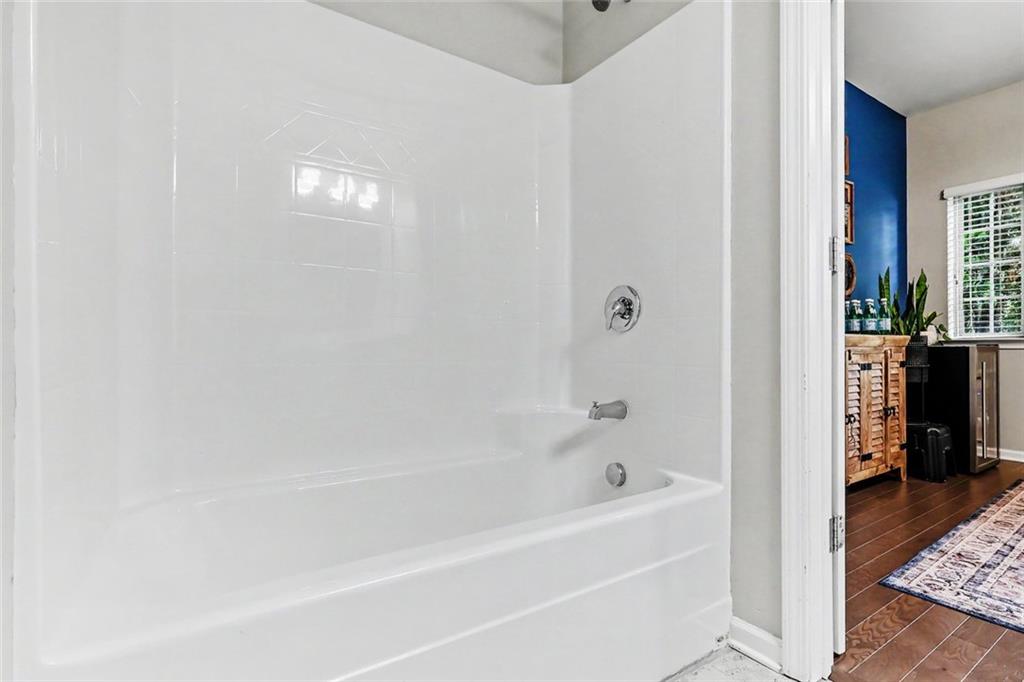 Bathroom bathtub with white surround and chrome fixtures, viewed through a doorway toward a blue-accented room.