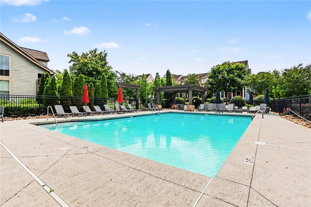 Outdoor swimming pool with a wide concrete deck, lounge chairs, and pergolas.