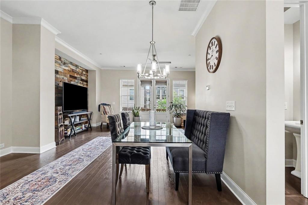 Dining area with a glass-top table and dark tufted chairs beside a living room with a wood accent wall.
