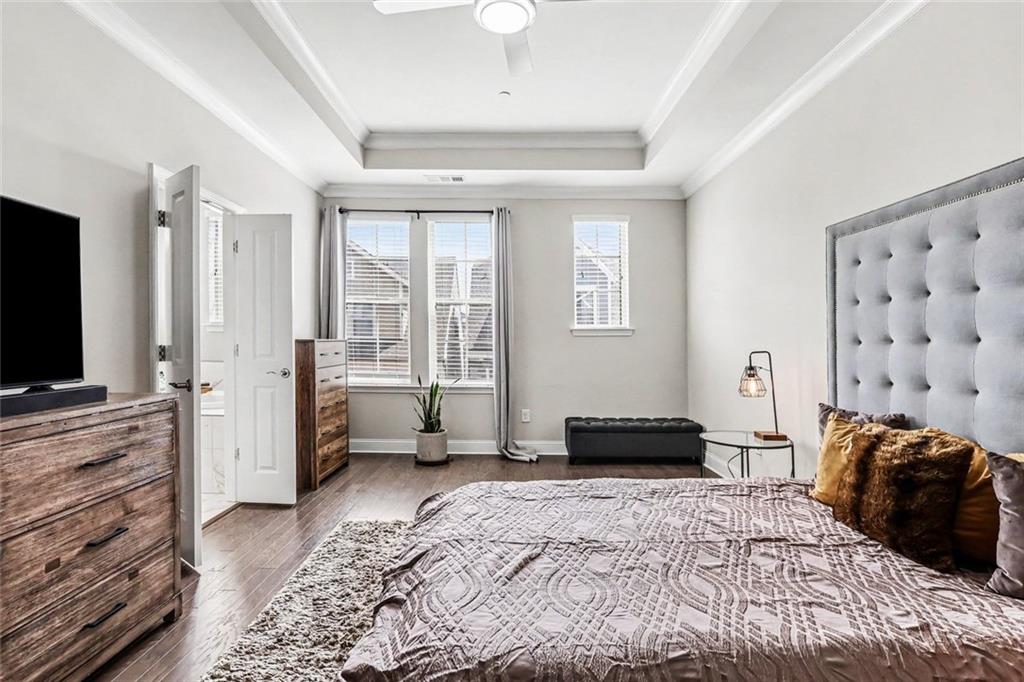 Bedroom with a tall tufted headboard, patterned bedding, and daylight through windows with blinds.