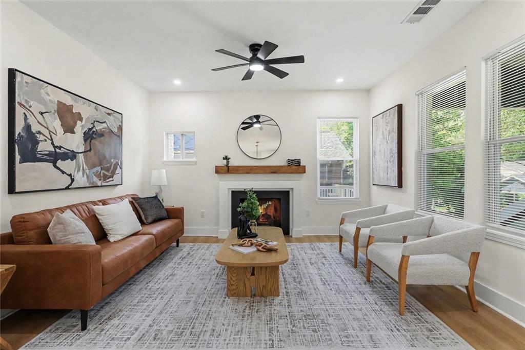 Staged living room with a fireplace, leather sofa, upholstered chairs, and large windows.