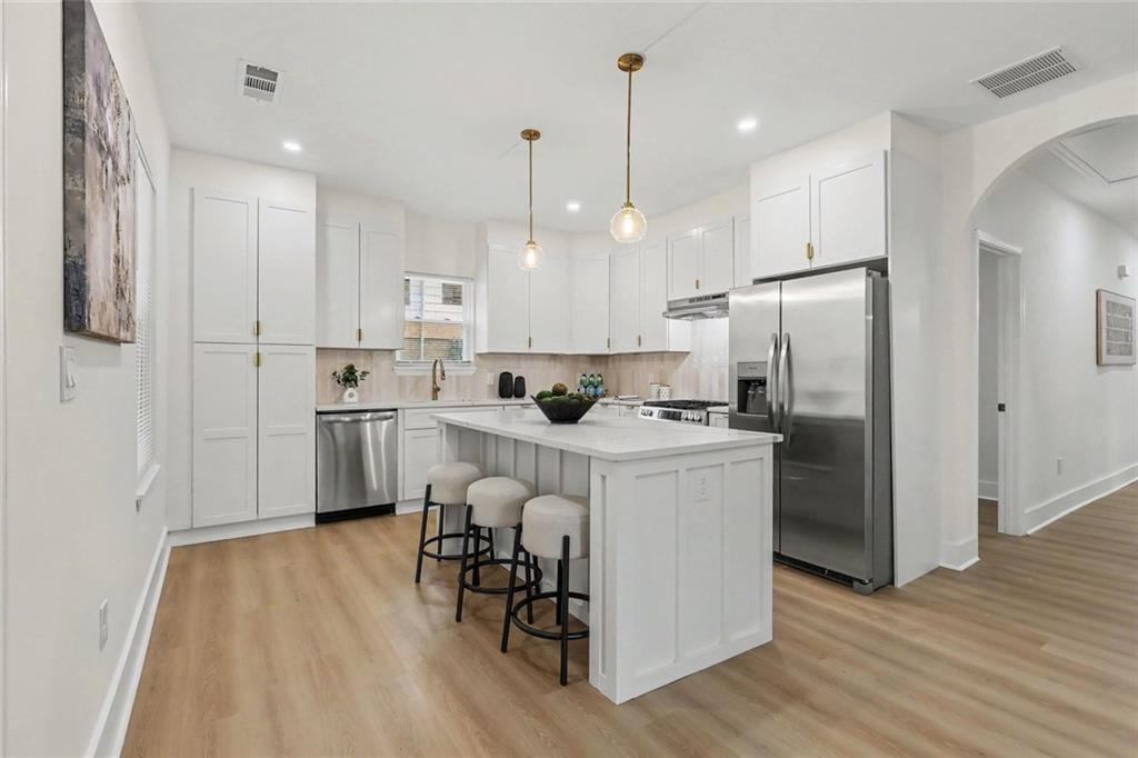 White kitchen with stainless steel appliances, a large island, and three upholstered stools.