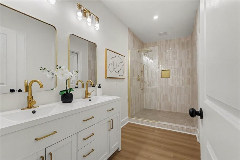 Bathroom with a double-sink vanity and gold fixtures beside a pale tiled glass shower.