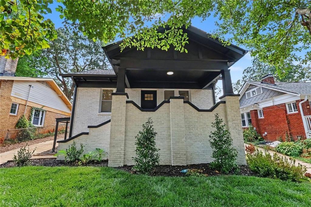 Light brick house with a deep covered porch, dark trim, and landscaped front lawn.