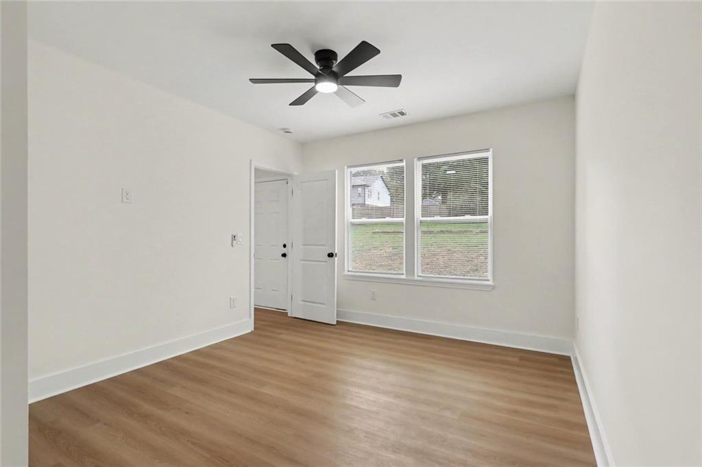 Empty room with light wood-look floors, two windows, and a dark ceiling fan.