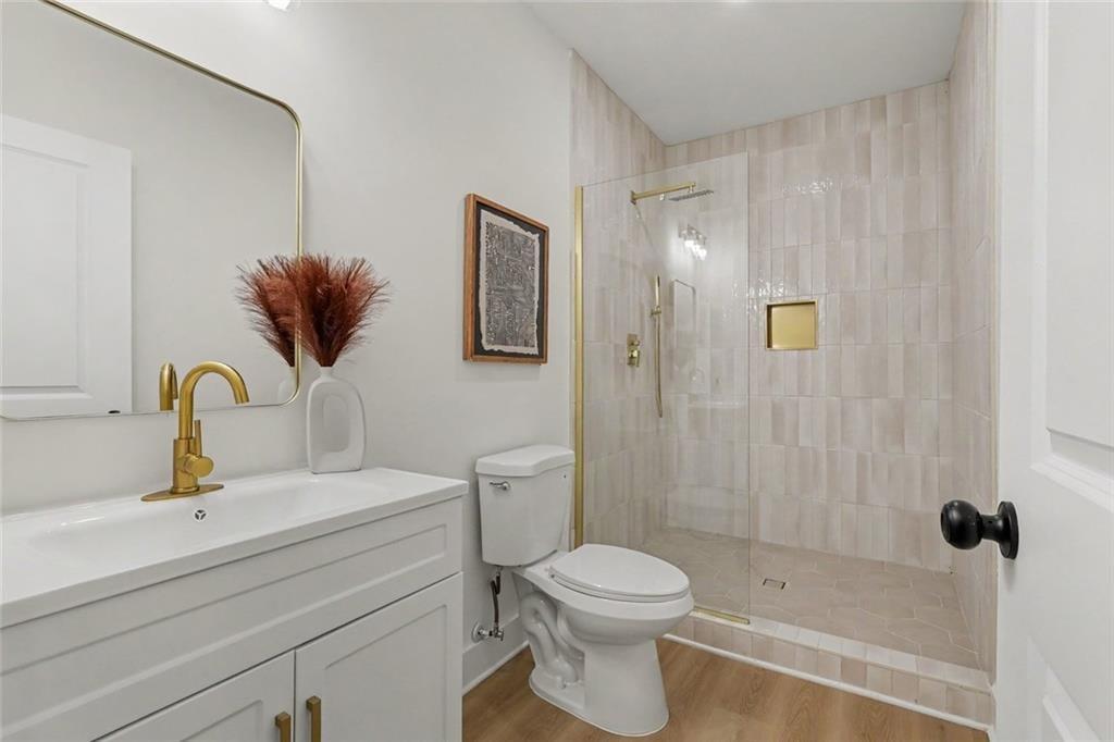 Bathroom with a white vanity, gold faucet, and pale tiled walk-in shower.