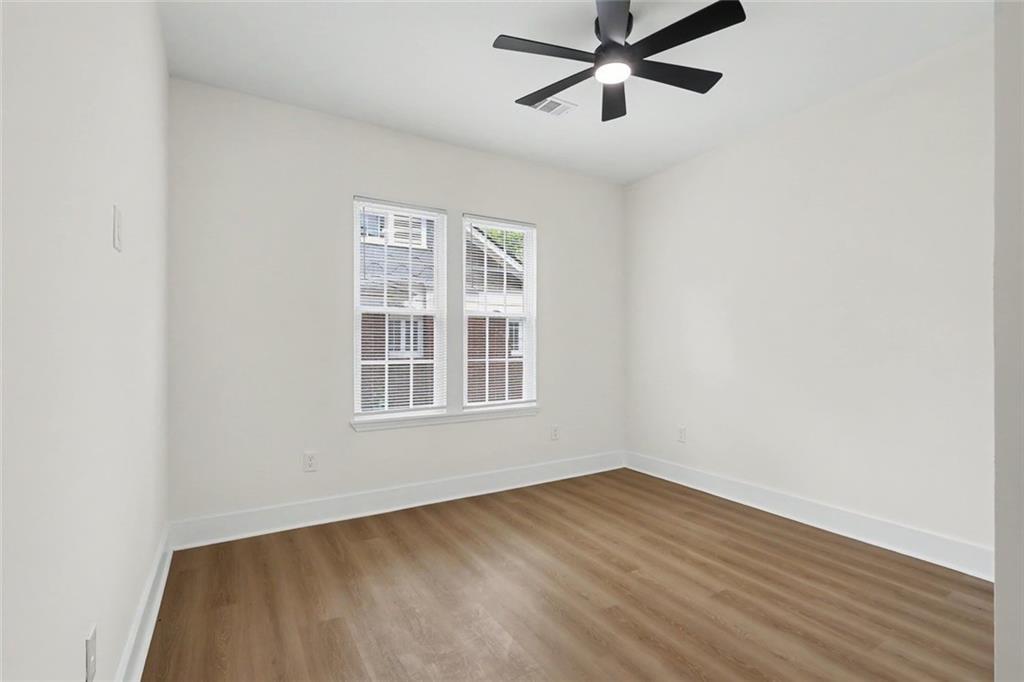 Vacant bedroom with wood-look flooring, two windows with blinds, and a black ceiling fan.