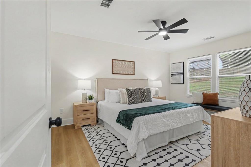 Staged bedroom with a white bed, teal throw, patterned rug, and windows with blinds.