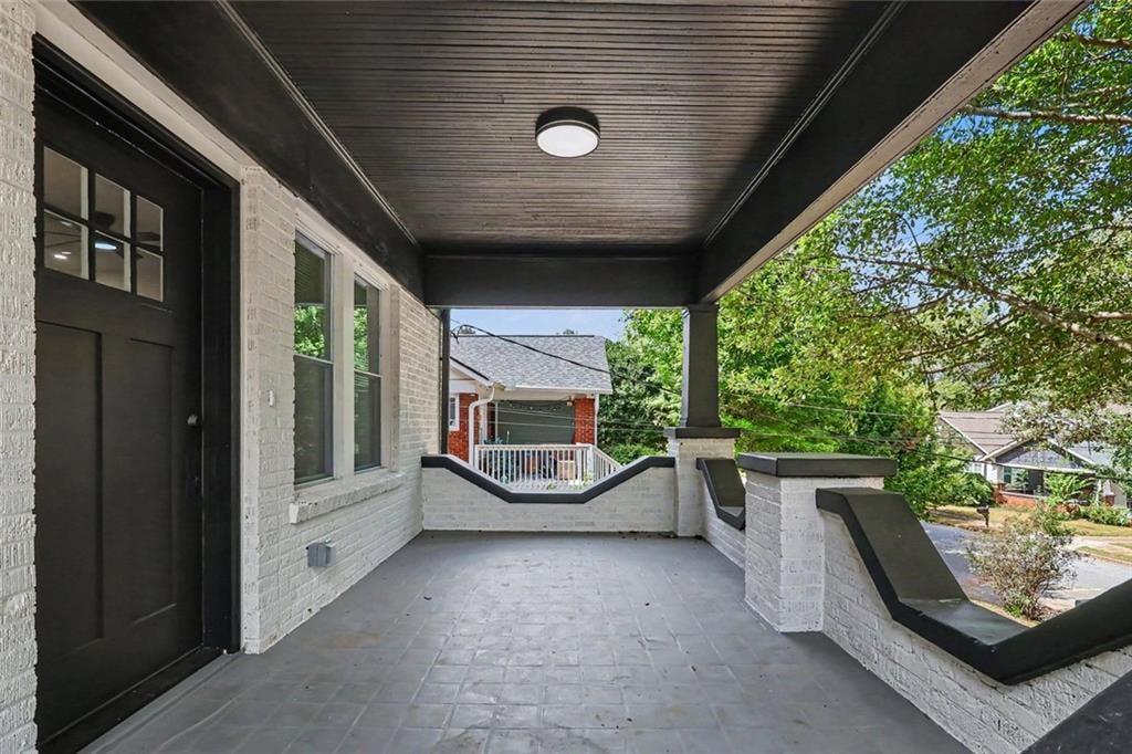 Covered front porch with white brick walls, black entry door, and dark-trimmed railing.