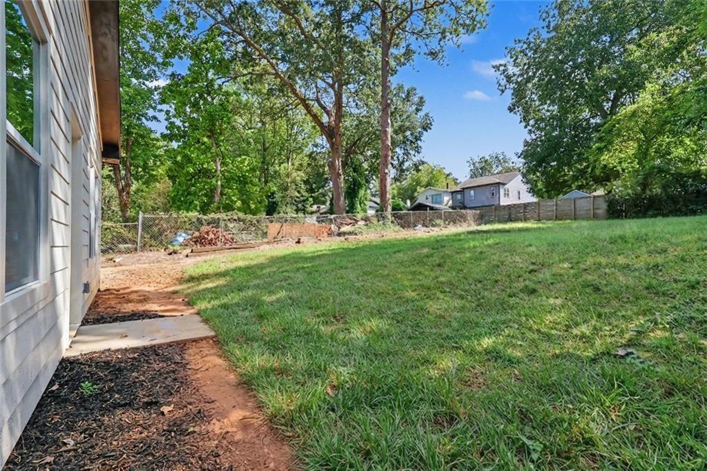 Grassy backyard with mature trees and a chain-link fence behind the house.