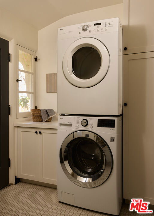 Laundry room with stacked front-loading washer and dryer beside built-in cabinets and a narrow window.