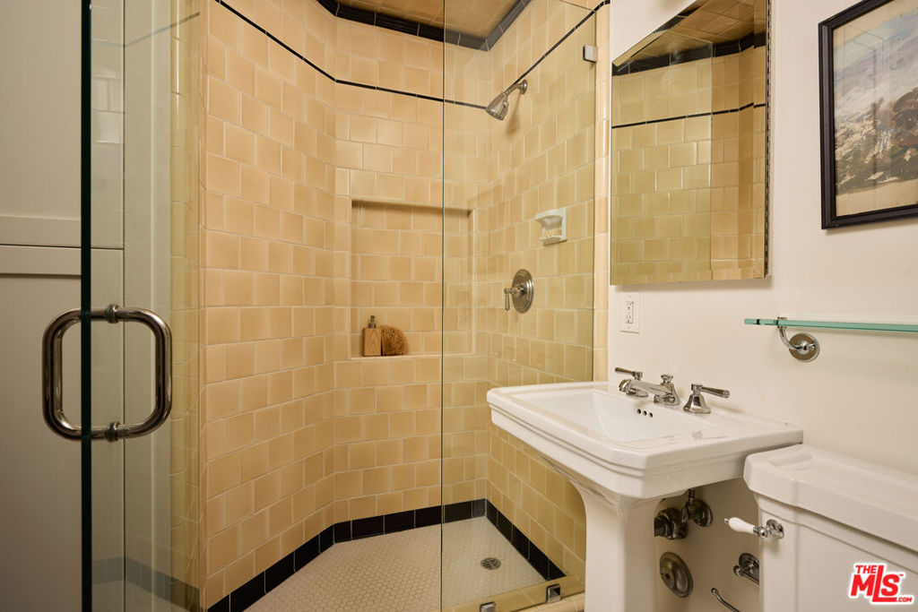 Bathroom with a tan-tiled glass shower, pedestal sink, and wall mirror.