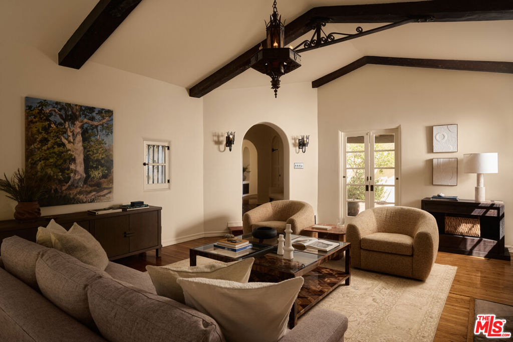 Living room with exposed ceiling beams, an arched doorway, and French doors.