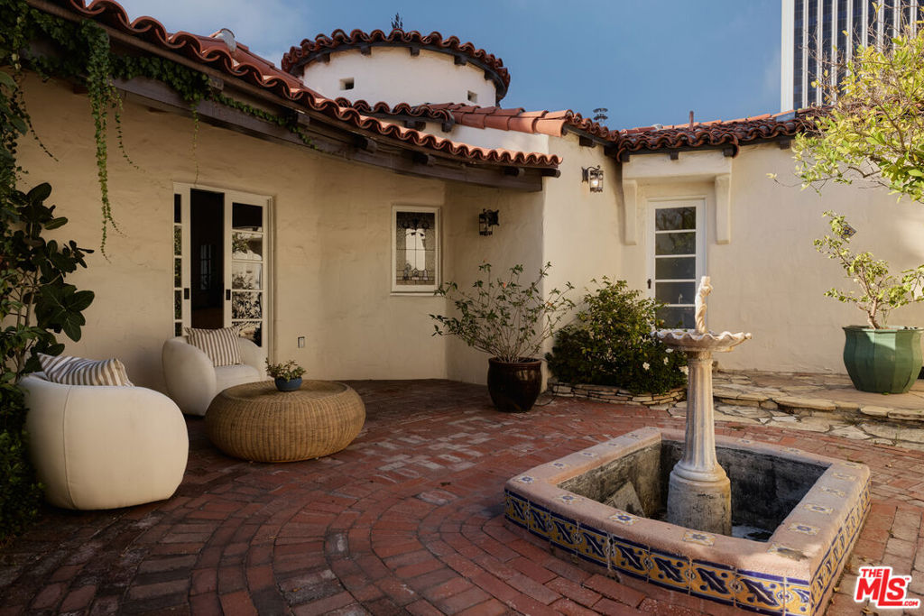 Spanish-style home courtyard with a tiled fountain, brick paving, and cushioned outdoor seating.
