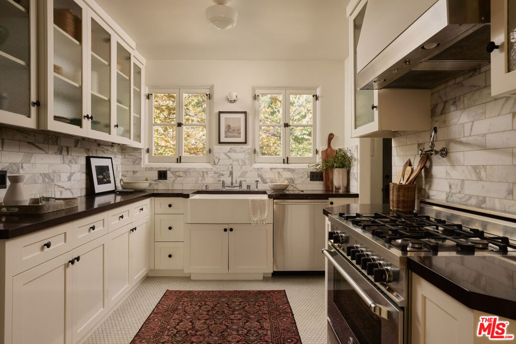 Kitchen with white cabinets, marble backsplash, farmhouse sink, and stainless-steel range.