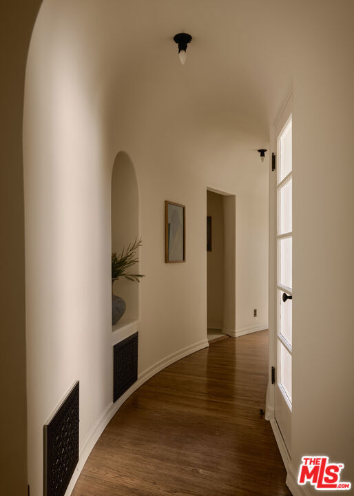 Curved hallway with hardwood floors, an arched display niche, framed artwork, and a glazed door.