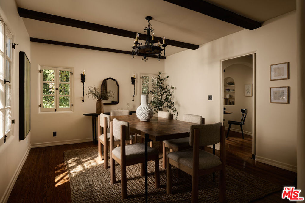 Dining room with a dark wood table, exposed ceiling beams, and sunlight streaming through the windows.