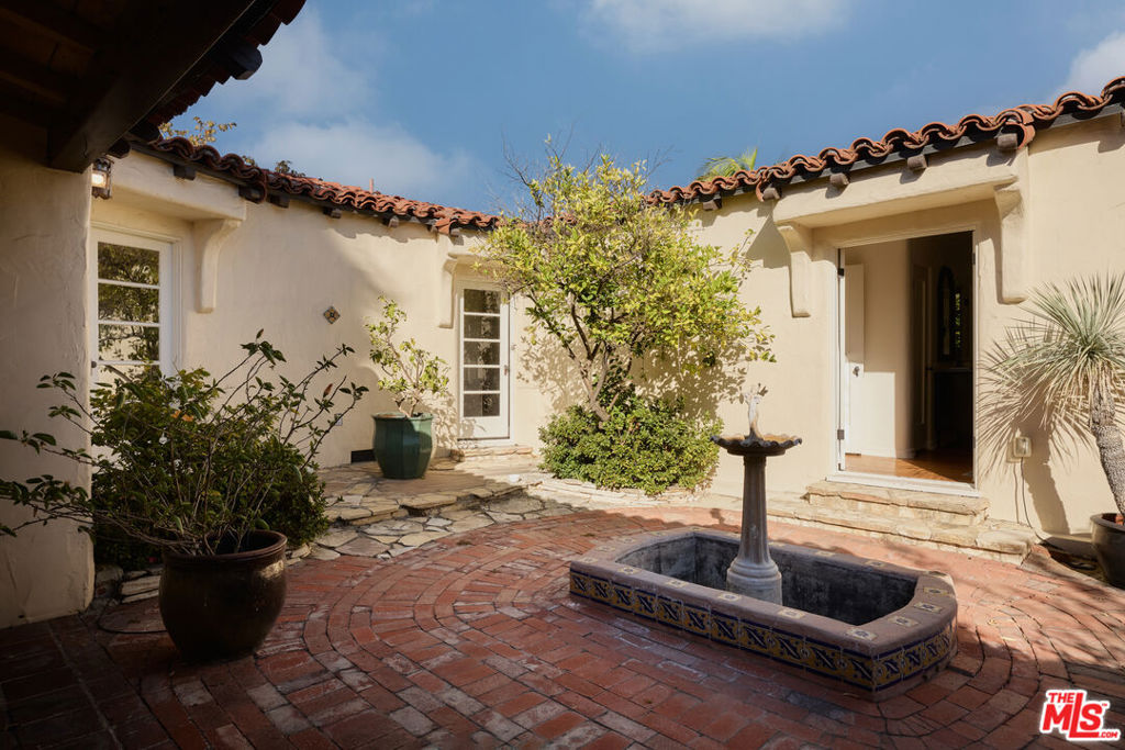 Spanish-style home courtyard with a tiled fountain basin, brick paving, and leafy plants.