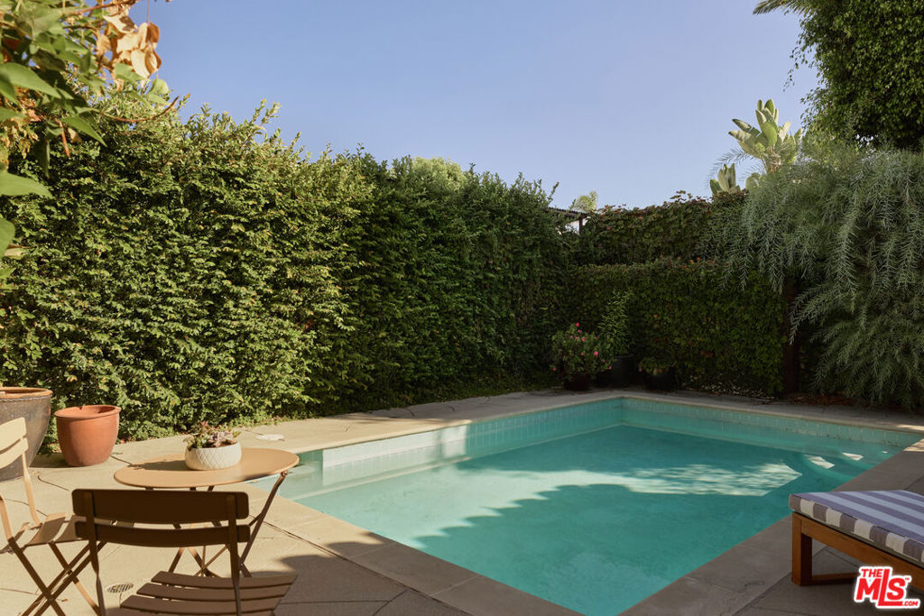 Backyard swimming pool bordered by tall hedges, with patio seating and tropical plants.