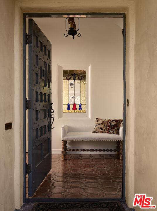 Entryway with a studded wooden door, terracotta tile floor, white bench, and stained-glass window.