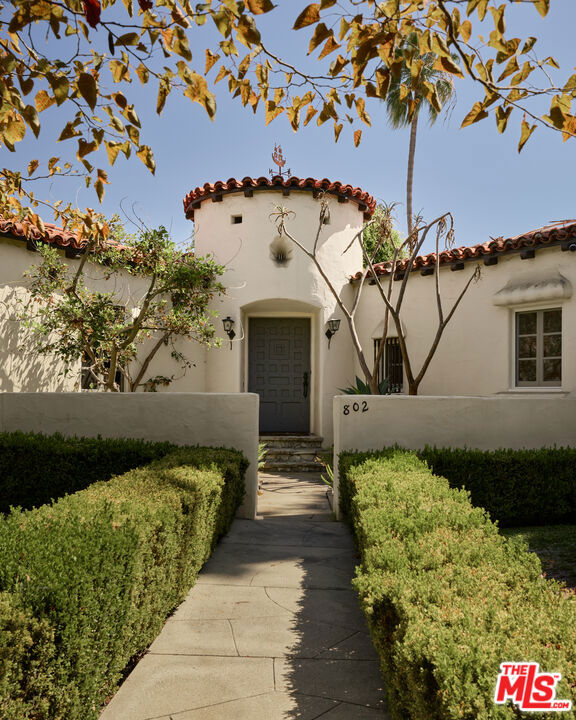 Spanish-style home with a red tile roof, arched entry, and hedge-lined walkway.