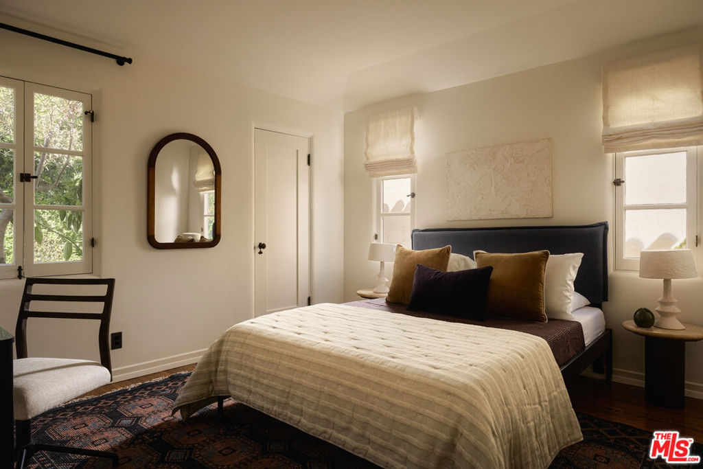 Furnished bedroom with a cream quilt, dark headboard, arched mirror, and patterned rug.