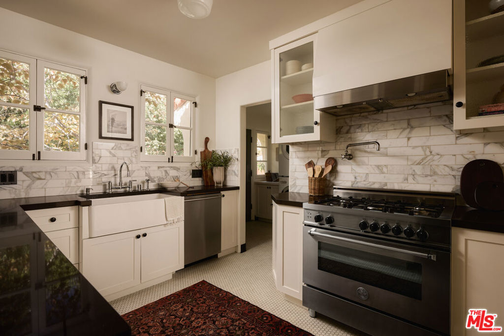 White kitchen with marble backsplash, farmhouse sink, and stainless-steel gas range.