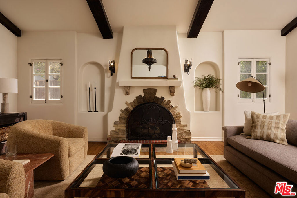 Living room with a stone fireplace, exposed ceiling beams, and seating around a glass coffee table.