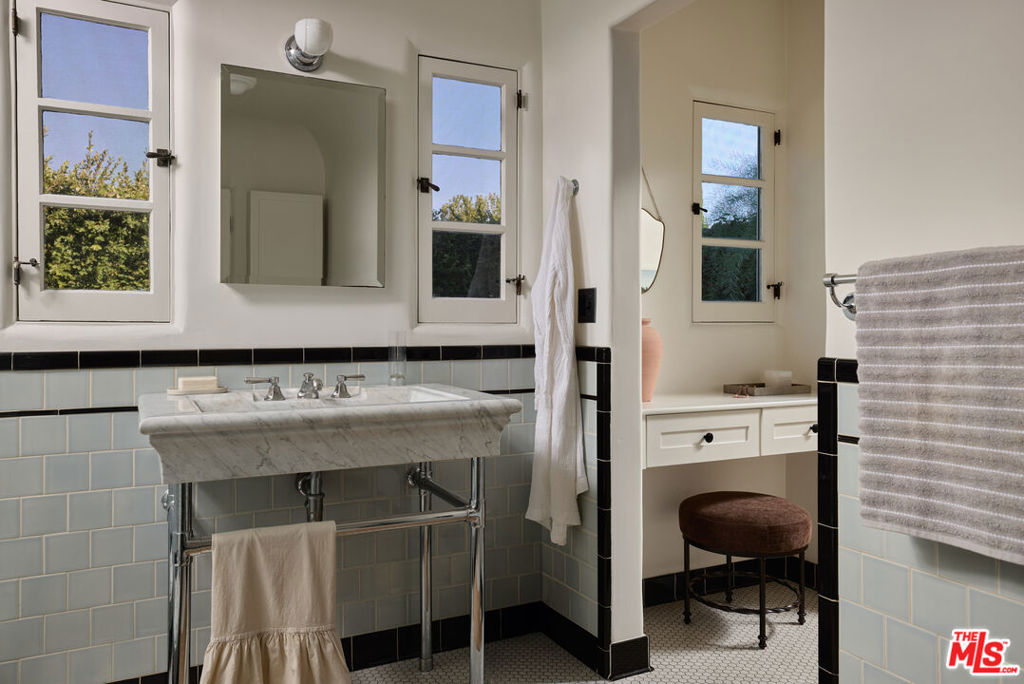 Bathroom with a marble sink, pale blue tiled walls, tall windows, and a separate vanity alcove.