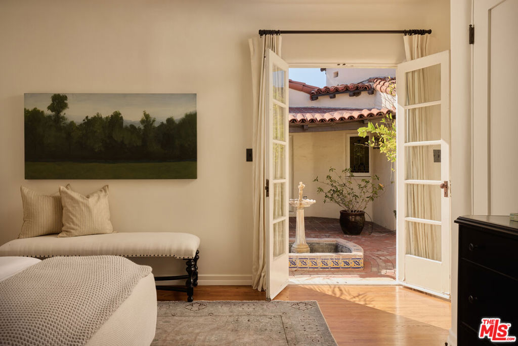 Bedroom with open French doors overlooking a brick courtyard and tiled fountain.