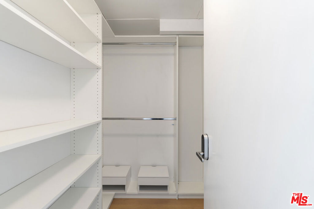 Empty walk-in closet with built-in white shelving, hanging rods, and two lower drawers.