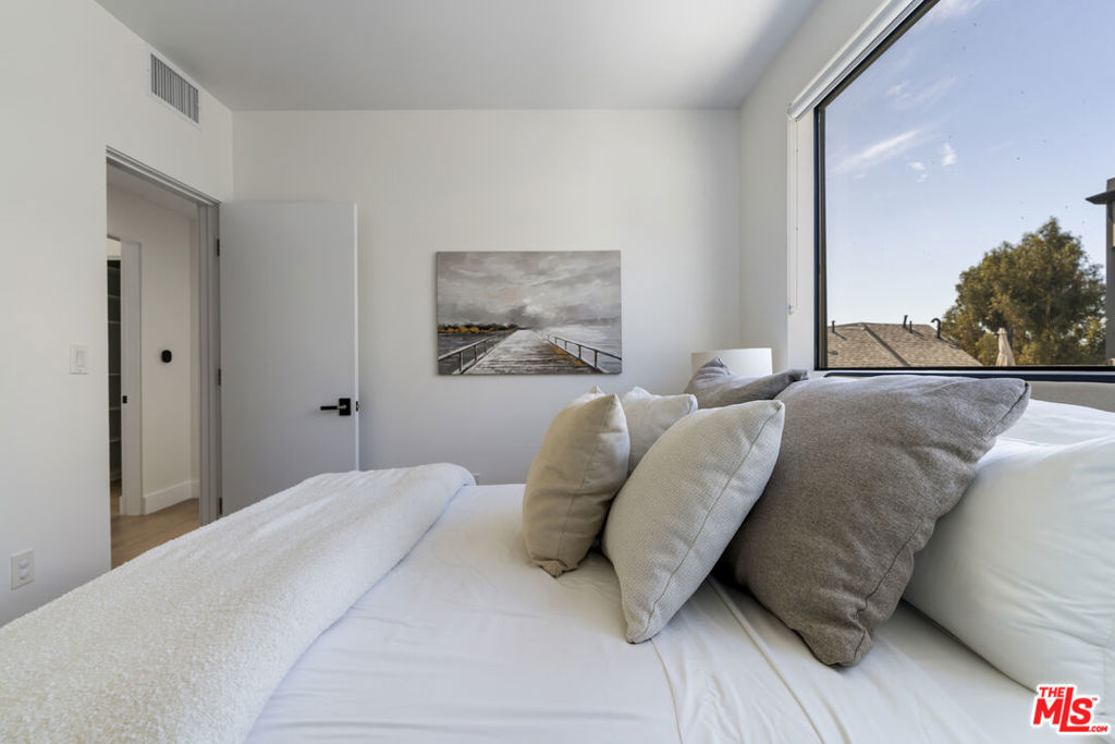 Staged bedroom with a white bed, layered neutral pillows, and a large window.