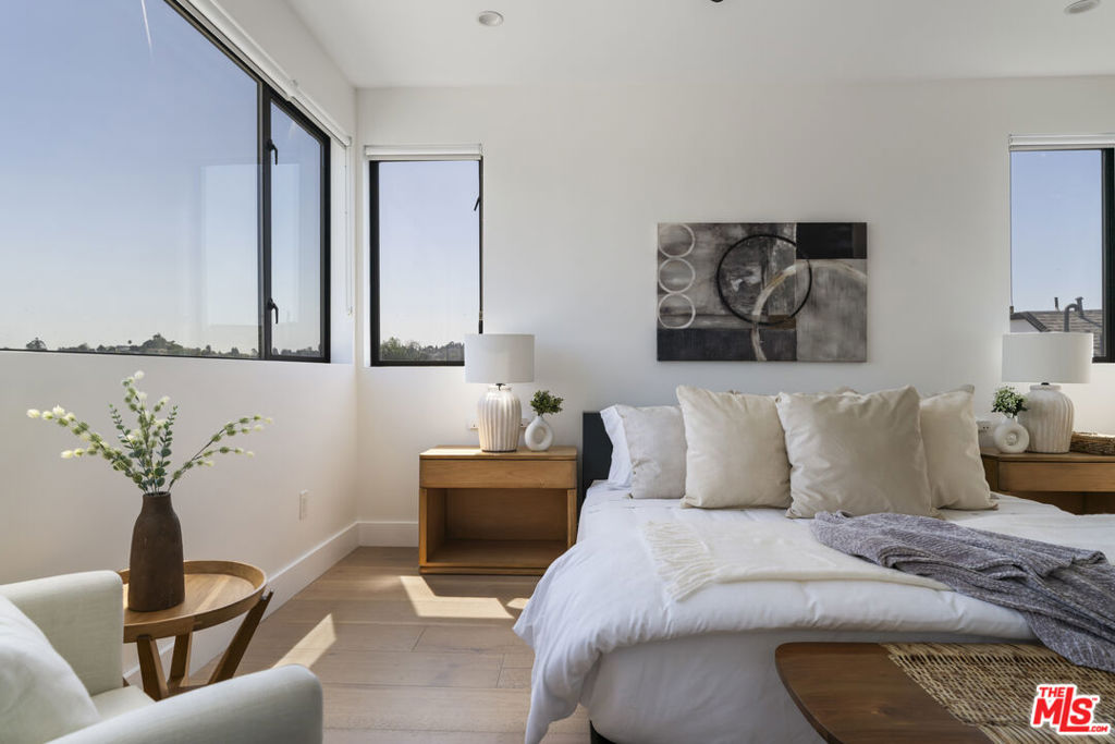 Bright staged bedroom with a white bed, abstract wall art, and large corner windows.