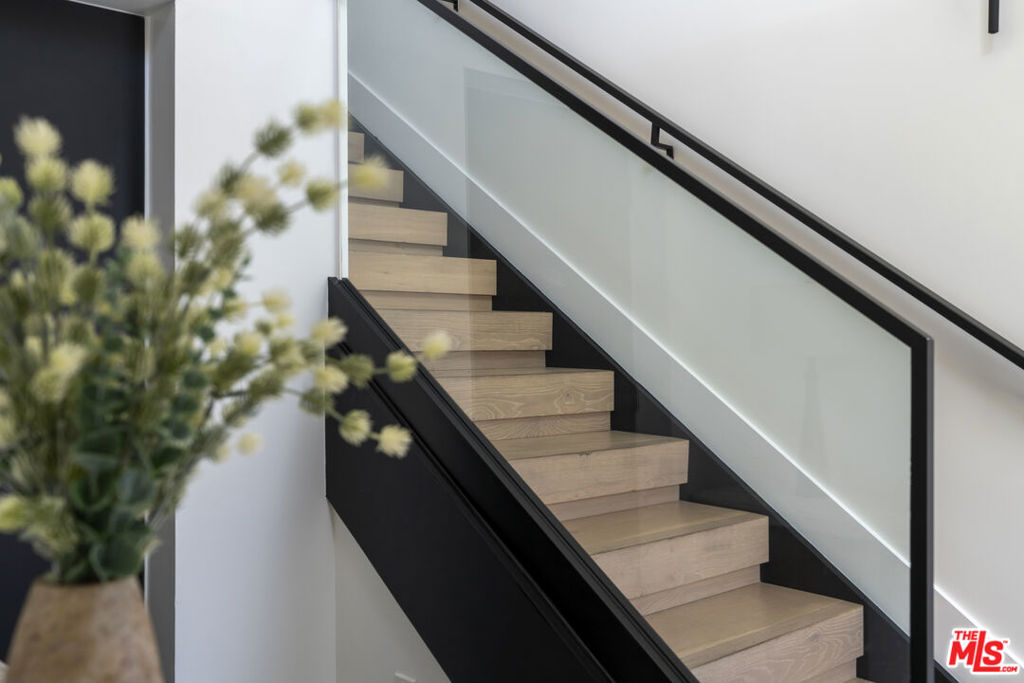 Modern staircase with light wood steps, black railings, and a glass balustrade.