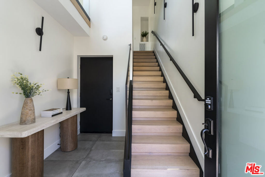 Entry hall with a light wood staircase, black railings, and a console table beside the dark front door.