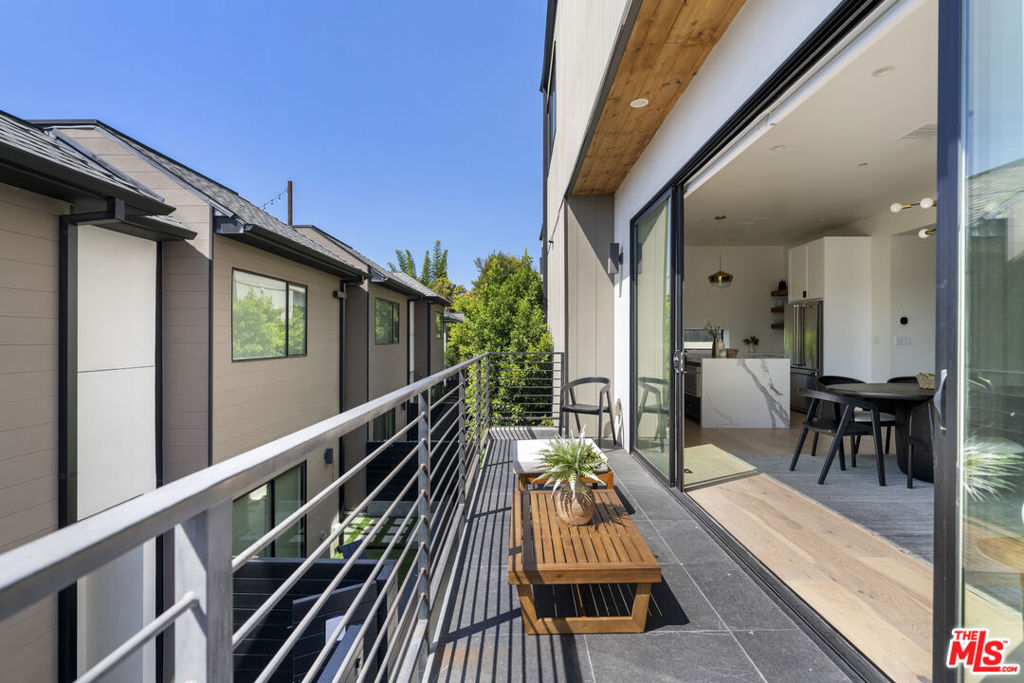 Apartment balcony with tiled floor, metal railing, and a wooden bench beside open sliding doors.
