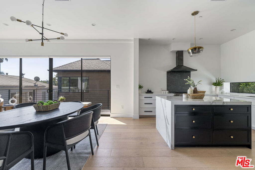 Modern kitchen with a marble island beside a black dining table and wide glass doors.