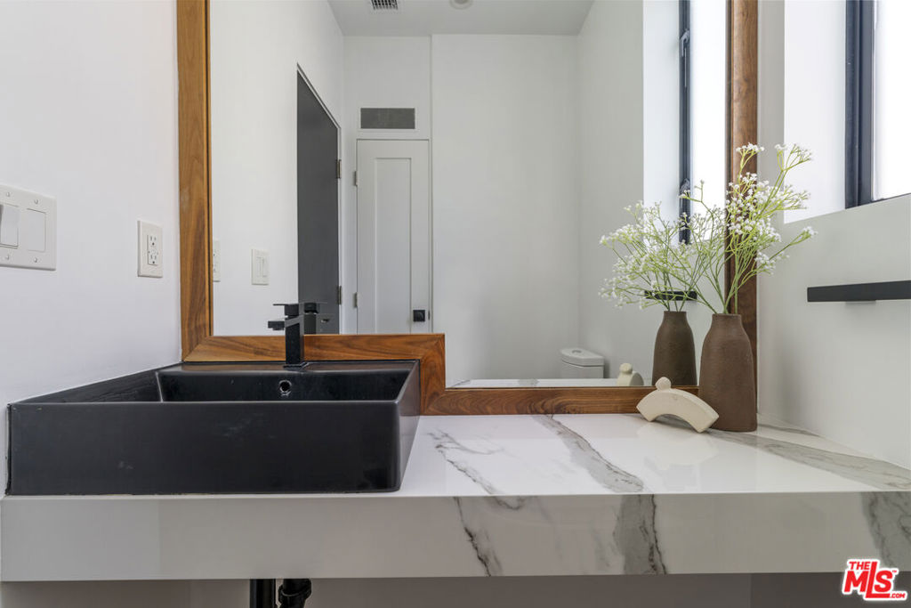 Bathroom vanity with a black vessel sink, marble-patterned counter, and wood-framed mirror.