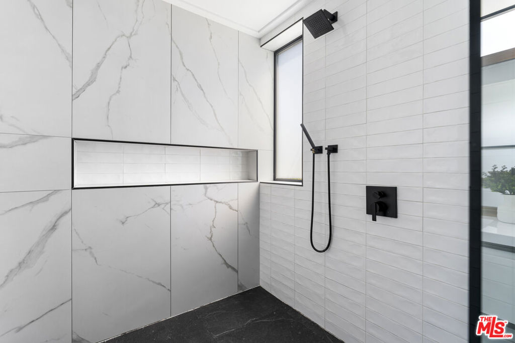 Bathroom shower with marble-look panels, a recessed niche, matte black fixtures, and a dark stone floor.