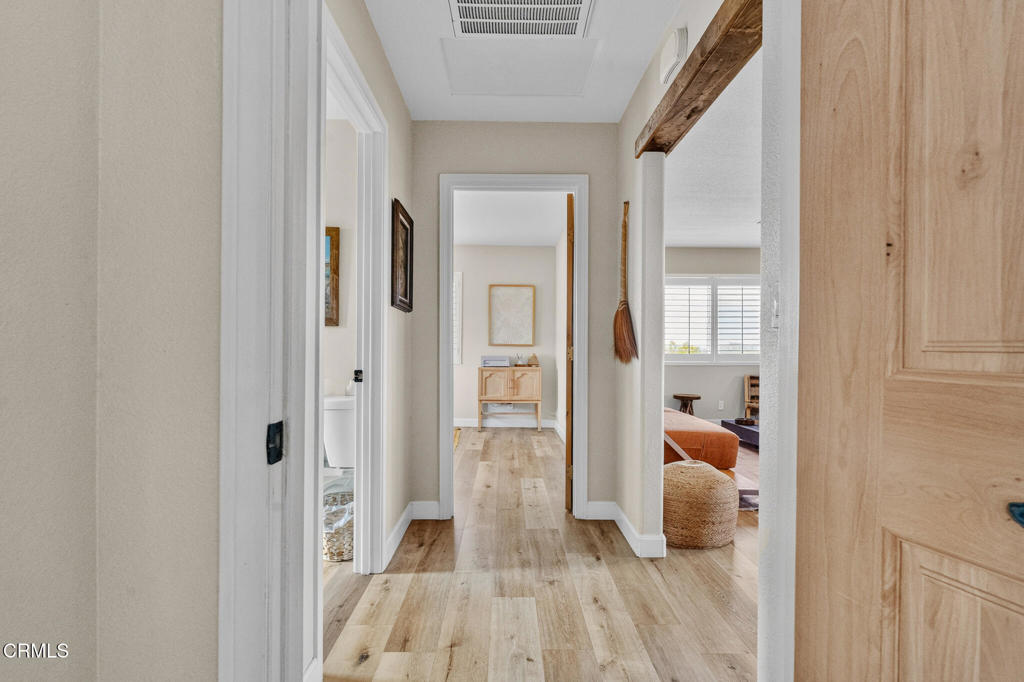 Hallway with light wood-look floors and open doorways to a bathroom and furnished rooms.