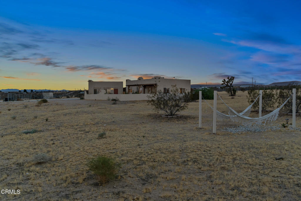 Modern desert home at dusk with a hammock in the sandy yard.
